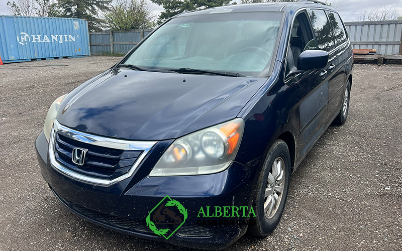Dark blue Honda Odyssey minivan in a dirt lot; Hanjin shipping container and wood fence in background.