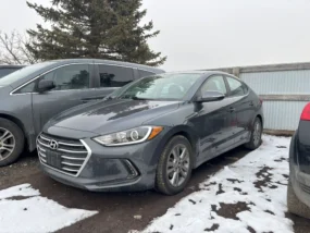 Gray Hyundai Elantra sedan parked in a snowy lot next to a gray minivan.