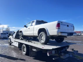 White Dodge Dakota 4x4 pickup on a flatbed tow truck under a clear blue sky.