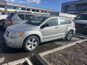 Silver Dodge Caliber in a parking lot on a sunny day with buildings in the background.