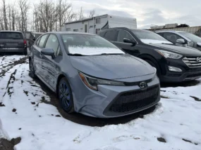 Gray Toyota Corolla parked in a snowy lot with other vehicles, on an overcast day.