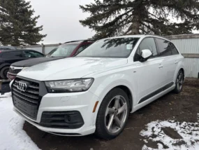 White Audi Q7 SUV parked in a muddy, snowy lot on a cloudy winter day.