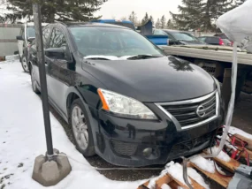 Black Nissan Sentra sedan in a snowy junk lot with other cars on an overcast day.
