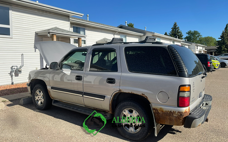 Rusty silver SUV with hood up, parked in apartment lot on sunny day. Alberta Cash For Cars logo.