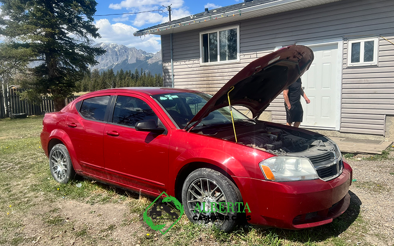 Red sedan with open hood parked beside a house in Alberta with mountains visible in the background