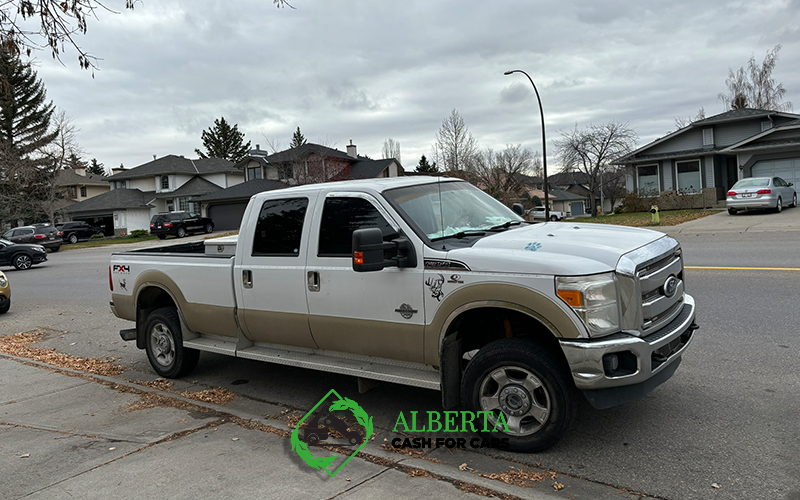 White and tan Ford F-250 pickup truck parked on a Calgary suburban street under cloudy skies; Alberta Cash for Cars logo.