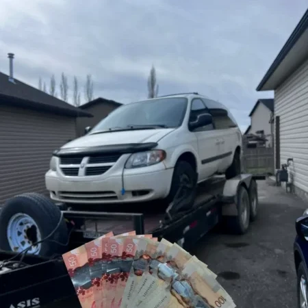 white dodge minivan loaded on a tow truck with Canadian cash displayed in the foreground during a cash for cars pickup service in a residential area